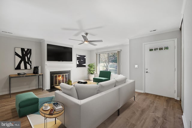 living area featuring a glass covered fireplace, baseboards, visible vents, and wood finished floors