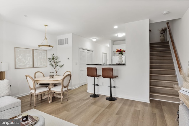 dining room featuring light wood-type flooring, visible vents, stairway, and baseboards