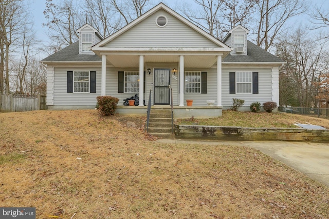 view of front facade featuring a porch, roof with shingles, a front lawn, and fence