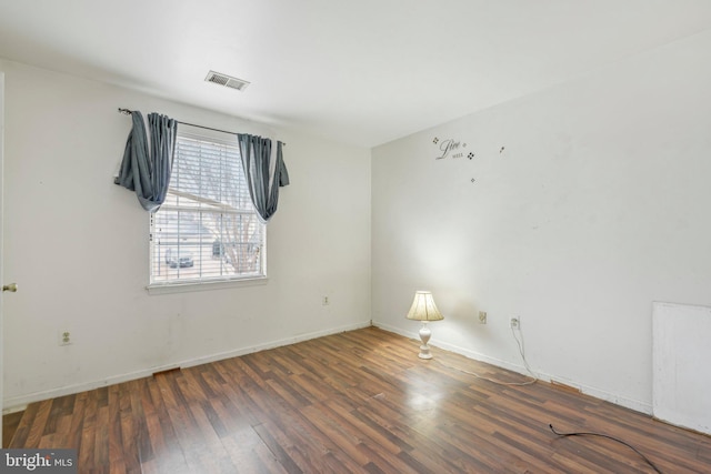 spare room with dark wood-style floors, visible vents, and baseboards