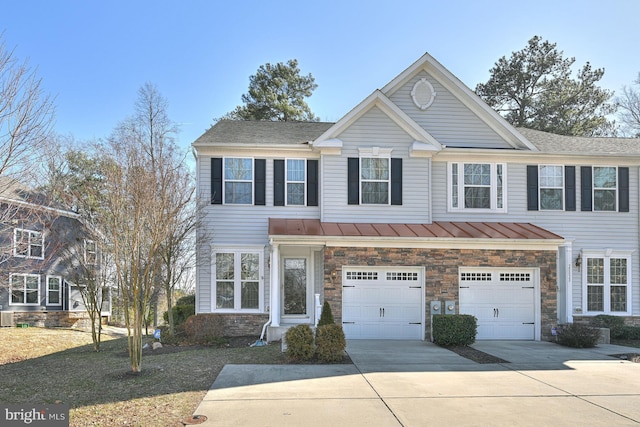 view of property featuring metal roof, an attached garage, driveway, stone siding, and a standing seam roof