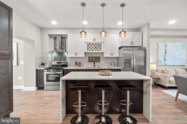 kitchen featuring a breakfast bar area, white cabinets, appliances with stainless steel finishes, light stone countertops, and wall chimney exhaust hood