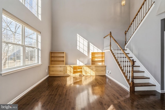 unfurnished living room featuring dark wood-style floors, a high ceiling, stairway, and baseboards