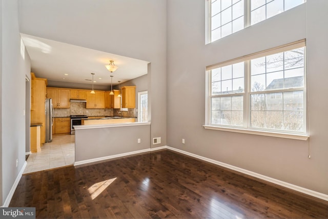 kitchen featuring appliances with stainless steel finishes, a peninsula, light brown cabinets, pendant lighting, and backsplash