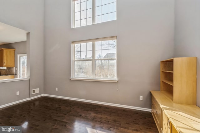 unfurnished living room featuring a towering ceiling, a wealth of natural light, baseboards, and dark wood-type flooring