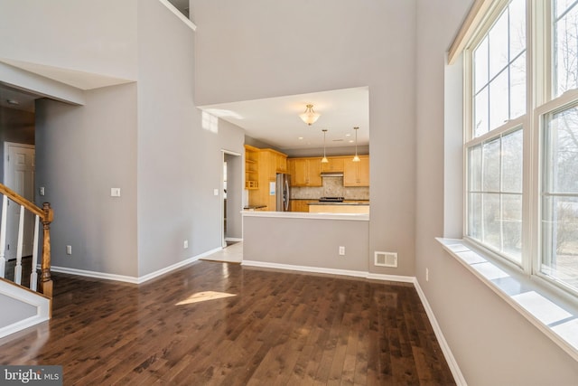 unfurnished living room with baseboards, visible vents, dark wood finished floors, a high ceiling, and stairs