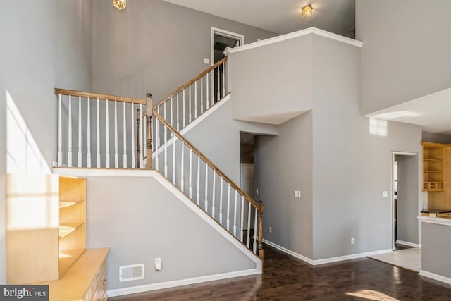 staircase featuring baseboards, a high ceiling, visible vents, and wood finished floors