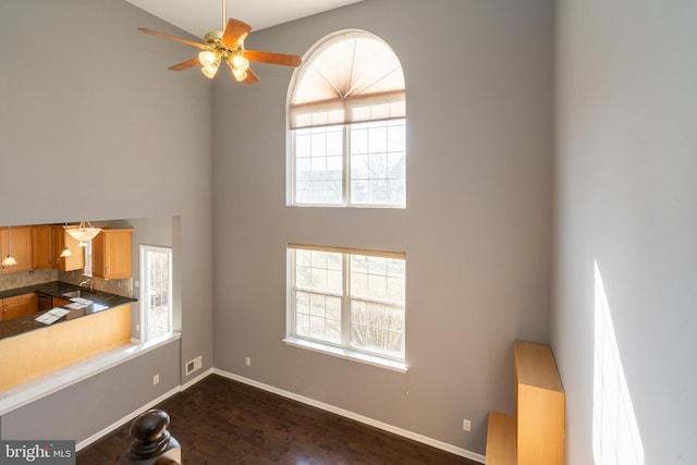 unfurnished living room featuring a high ceiling, a sink, a ceiling fan, and baseboards