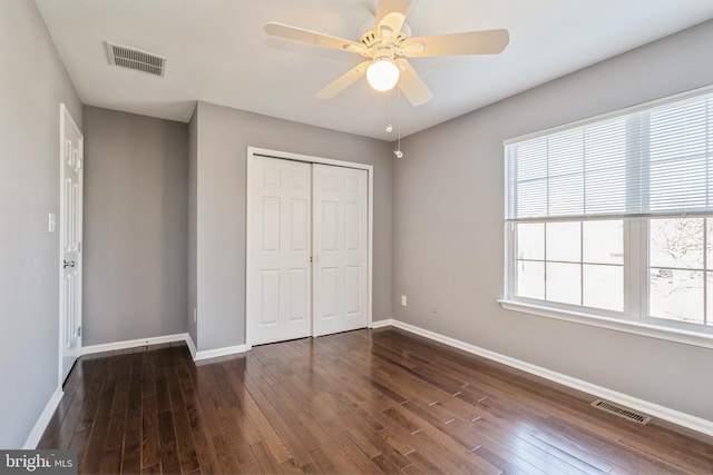 unfurnished bedroom with dark wood-type flooring, a closet, visible vents, and baseboards