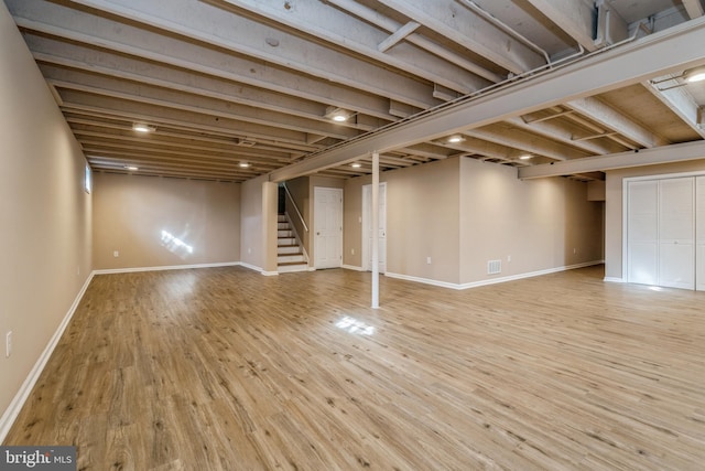 finished basement featuring light wood-type flooring, visible vents, baseboards, and stairs