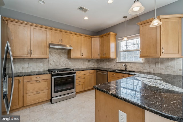 kitchen featuring dark stone countertops, decorative light fixtures, stainless steel appliances, under cabinet range hood, and a sink