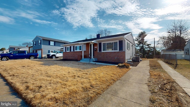 view of front of home with cooling unit, brick siding, fence, a front lawn, and a chimney