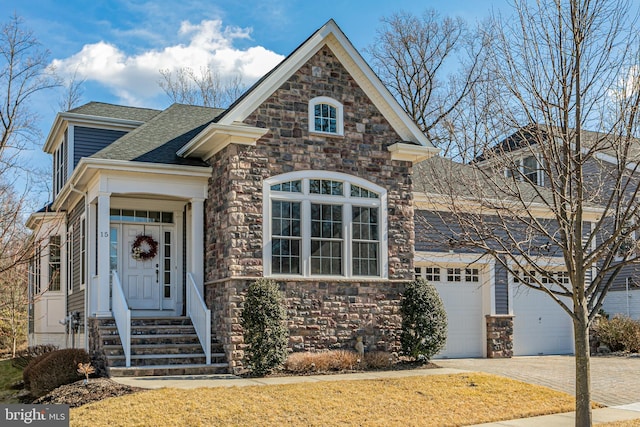 view of front of home with a garage, driveway, a shingled roof, and stone siding