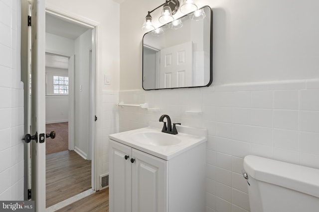 bathroom featuring toilet, a wainscoted wall, wood finished floors, vanity, and tile walls