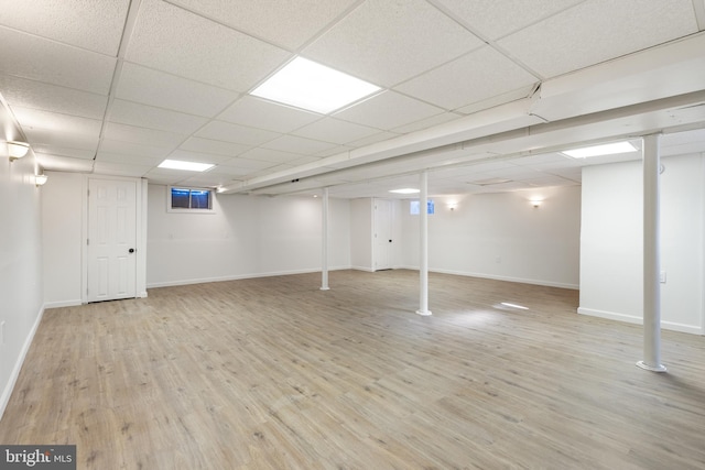 finished below grade area with baseboards, a drop ceiling, and light wood-style floors