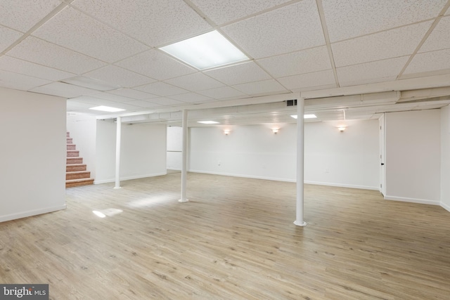 finished basement featuring wood finished floors, a drop ceiling, baseboards, and stairs