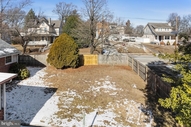 yard layered in snow featuring a fenced backyard and a residential view