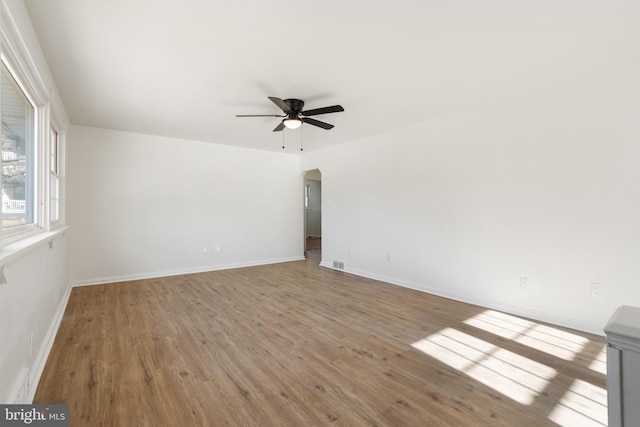 unfurnished room with light wood-style flooring, arched walkways, ceiling fan, and baseboards