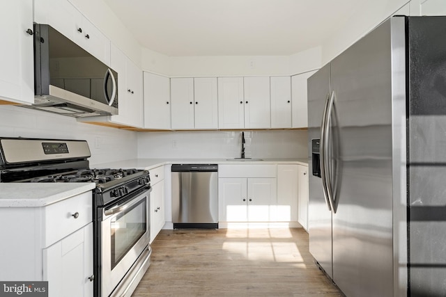 kitchen featuring stainless steel appliances, light countertops, light wood-style flooring, white cabinets, and a sink