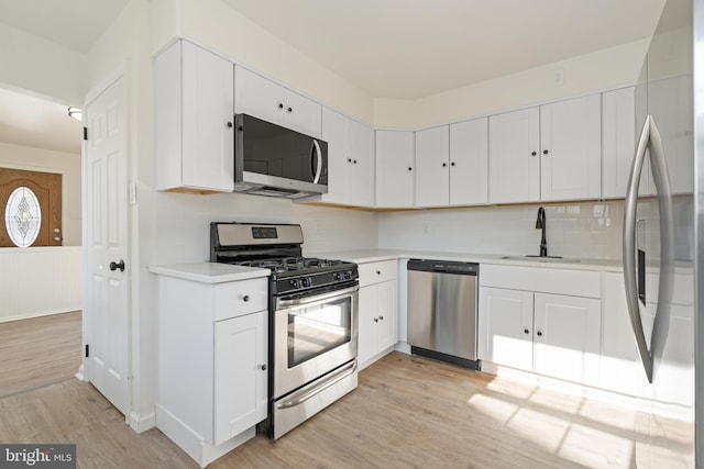 kitchen with stainless steel appliances, light countertops, white cabinets, a sink, and light wood-type flooring