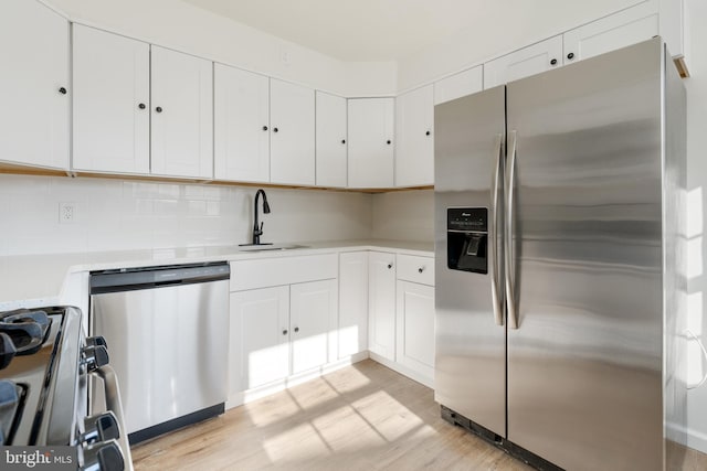 kitchen featuring light wood finished floors, white cabinets, stainless steel appliances, light countertops, and a sink