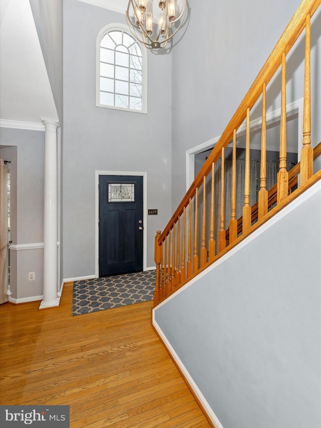 foyer entrance featuring a high ceiling, wood finished floors, baseboards, stairway, and decorative columns