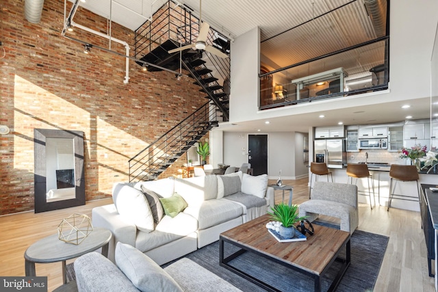 living area with a towering ceiling, light wood finished floors, brick wall, and stairway