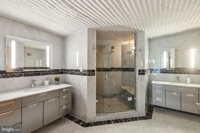 full bath featuring a stall shower, two vanities, a sink, and tile walls