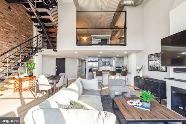 living area featuring stairway, light wood-style floors, a fireplace, and a towering ceiling