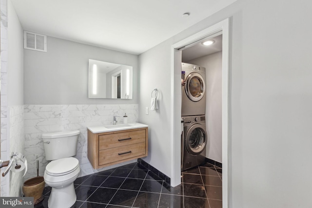 bathroom featuring tile patterned flooring, toilet, visible vents, vanity, and stacked washer and clothes dryer