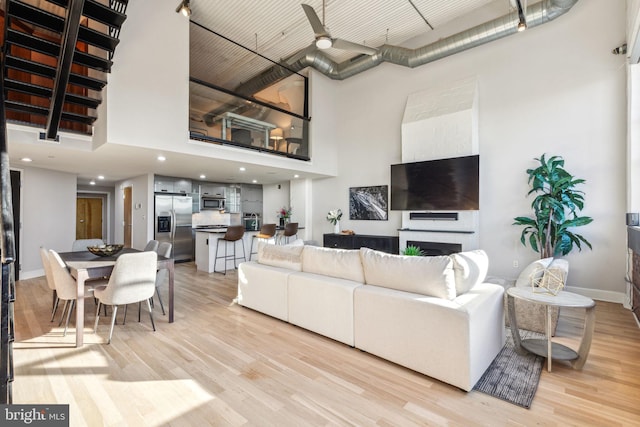 living area featuring baseboards, a fireplace, a towering ceiling, and light wood-style floors