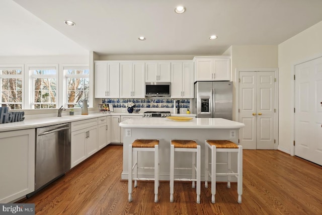 kitchen with a center island, appliances with stainless steel finishes, white cabinetry, wood finished floors, and a kitchen bar