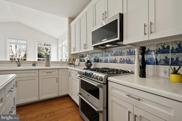 kitchen with white cabinets, light wood-style flooring, vaulted ceiling, stainless steel appliances, and light countertops