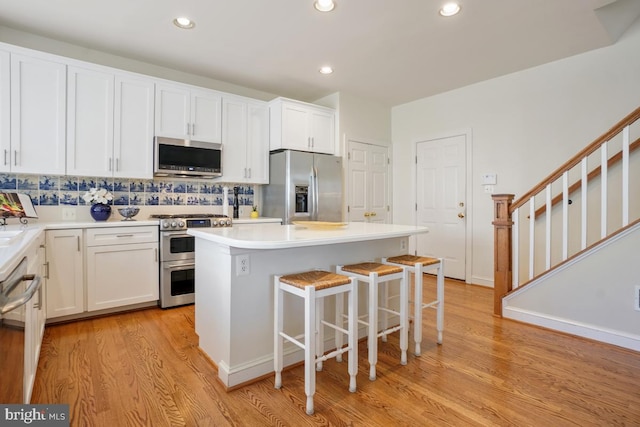 kitchen featuring appliances with stainless steel finishes, a kitchen breakfast bar, light wood-type flooring, white cabinetry, and recessed lighting