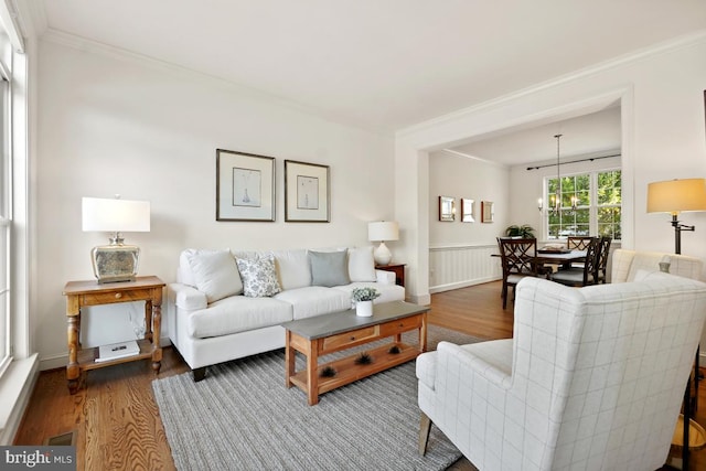 living area with a notable chandelier, wainscoting, wood finished floors, and crown molding