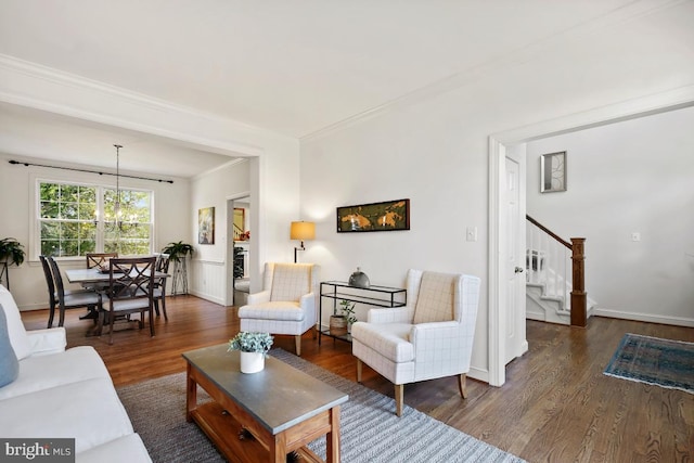 living room with a notable chandelier, stairway, ornamental molding, wood finished floors, and baseboards