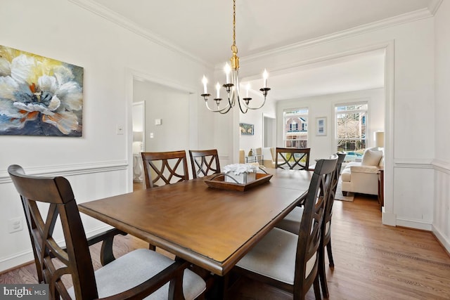 dining area with light wood-style floors, baseboards, ornamental molding, and an inviting chandelier