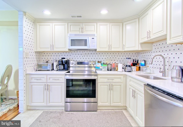 kitchen featuring stainless steel appliances, a sink, visible vents, light countertops, and decorative backsplash