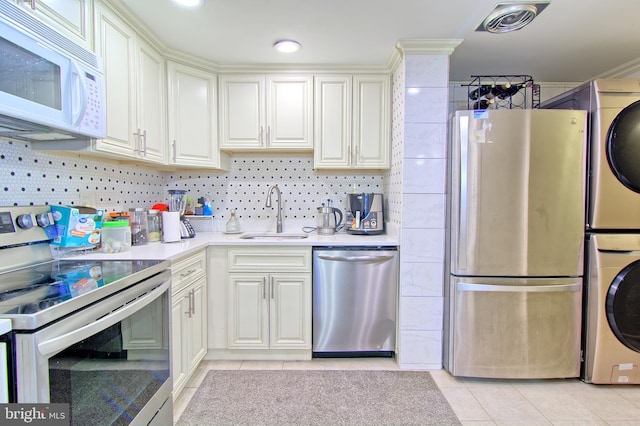 kitchen featuring stainless steel appliances, stacked washer / drying machine, light countertops, visible vents, and a sink