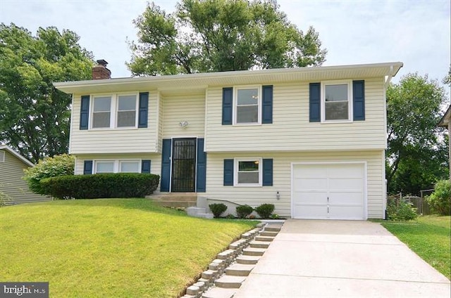 split foyer home featuring concrete driveway, an attached garage, a chimney, and a front lawn