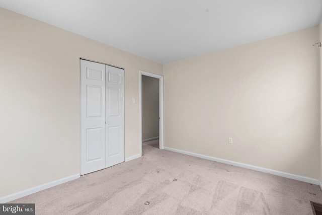 unfurnished bedroom with light carpet, baseboards, and a closet