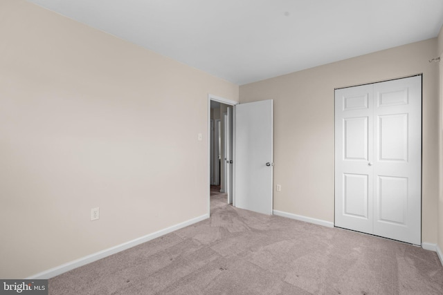 unfurnished bedroom with light carpet, a closet, and baseboards