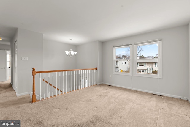 spare room featuring baseboards, a notable chandelier, and light colored carpet