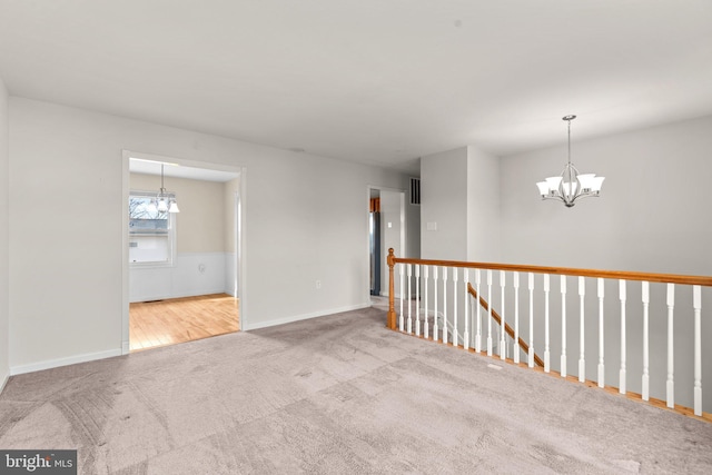 spare room featuring baseboards, light colored carpet, and a notable chandelier