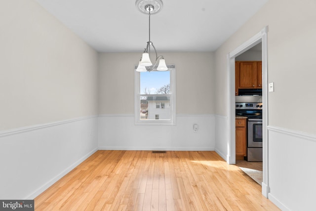 unfurnished dining area featuring a chandelier, light wood-type flooring, and baseboards