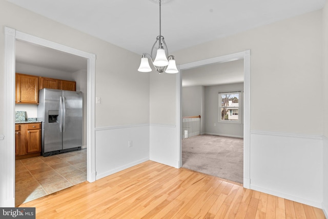 unfurnished dining area with light wood-type flooring, light carpet, baseboards, and an inviting chandelier