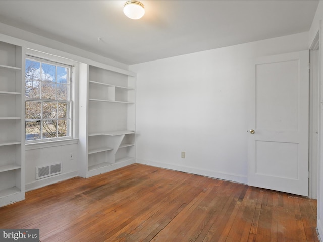 unfurnished room featuring built in shelves, wood finished floors, visible vents, and baseboards