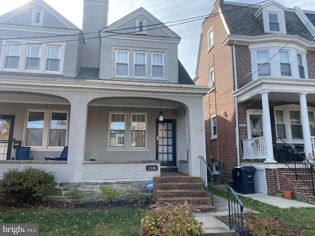 view of front of home with covered porch, a chimney, and stucco siding