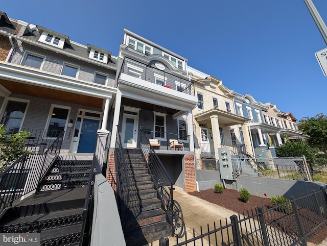 multi unit property with brick siding, a fenced front yard, stairway, and mansard roof