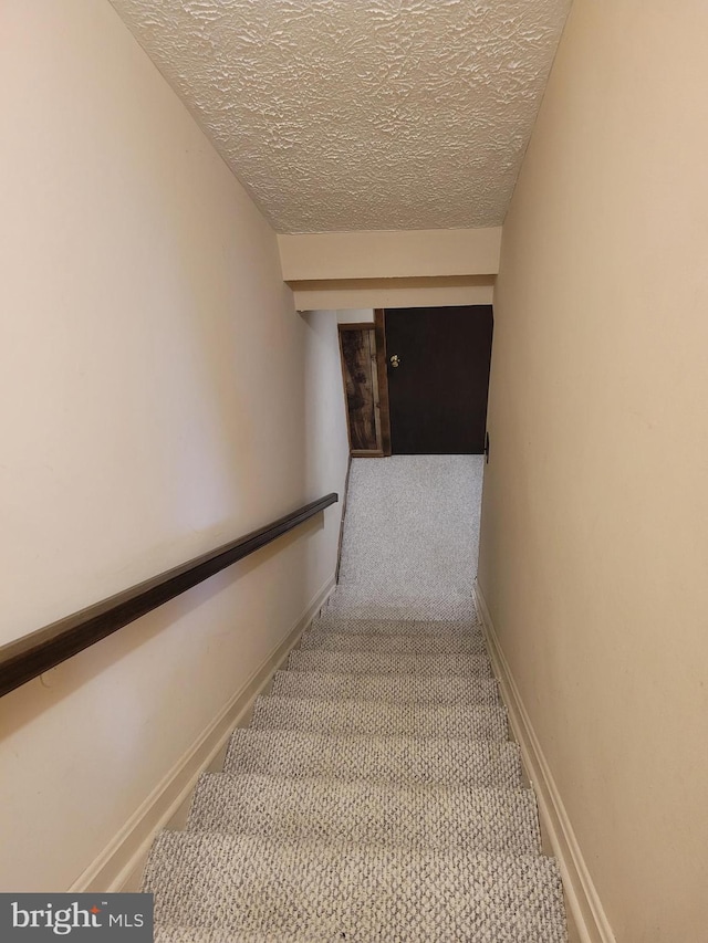 stairs featuring a textured ceiling, carpet floors, and baseboards